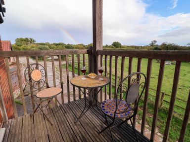 A balcony with a table and chairs overlooking a field at Hayloft in Ipswich