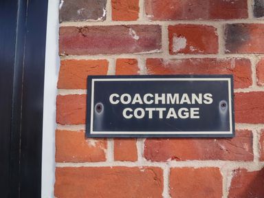 A sign that says COACHMANS COTTAGE on a brick wall at Coachman's Cottage Ipswich