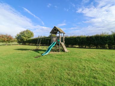 A playground with a slide and swings in a grassy area at Coachman's Cottage in Ipswich