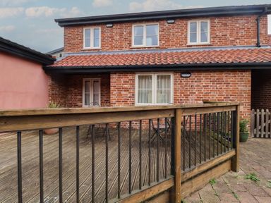 An outdoor area with a wooden deck and a two-story brick building at Blacksmith's Cottage Ipswich