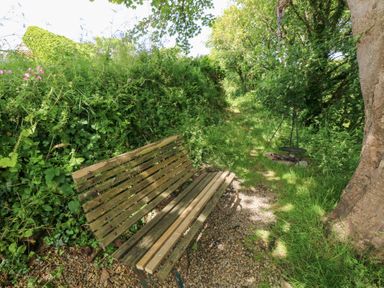 A bench beside a path with trees and grass at The Shephard Hut Nine Wells near Solva