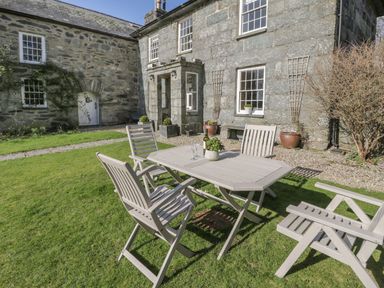 A garden with a table and chairs in front of a stone building at Bwthyn Morse Llanfair