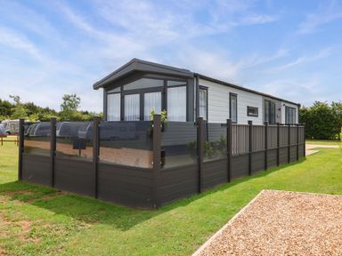 A caravan with a surrounding fence and grass area at Hazelnut Lodge in Chipping Norton