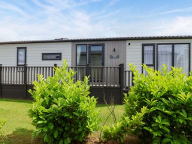 A mobile home with a deck and bushes at Hazelnut Lodge in Chipping Norton