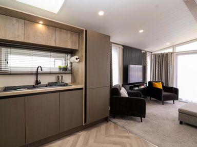 A living room with kitchen area featuring a sink and television at Hazelnut Lodge in Chipping Norton
