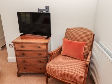 A bedroom with a television on a chest of drawers and an armchair at Watermill Cottage North Charlton