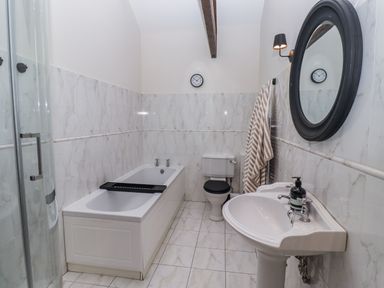 A bathroom with a bathtub, shower, toilet, and sink at Watermill Cottage in North Charlton