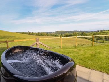A hot tub with water and a scenic landscape at Defaid Cymreig Oswestry