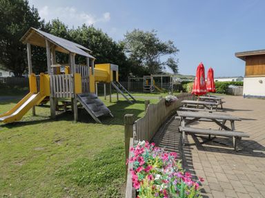 An outdoor play area with a playground and picnic tables at Puffin Way Holiday Caravan 