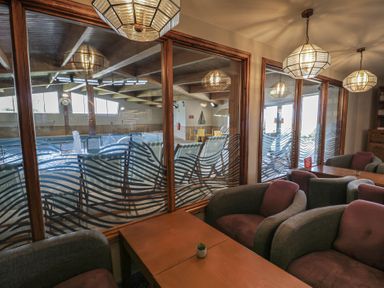 A seating area with chairs and tables overlooking an indoor pool at Puffin Way Holiday Caravan
