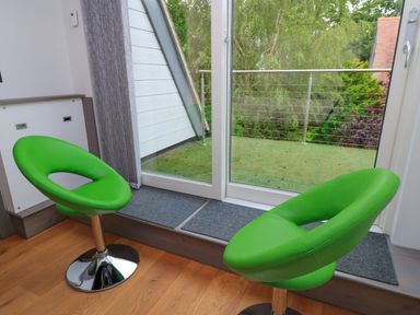 A living room with green chairs and a glass door leading to a balcony at Silver Copse in Frilford Heath Near Abingdon