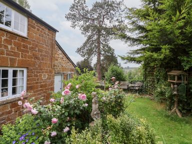 A garden with flowers and benches at Magdalen Cottage in Hook Norton