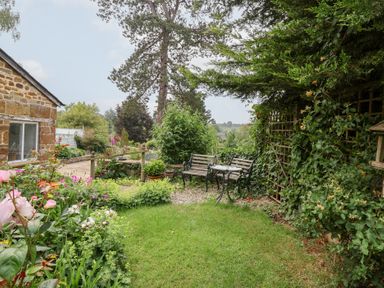 A garden with flowers, benches and a table at Magdalen Cottage in Hook Norton