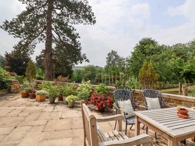 A garden with a table and chairs surrounded by plants at Magdalen Cottage in Hook Norton