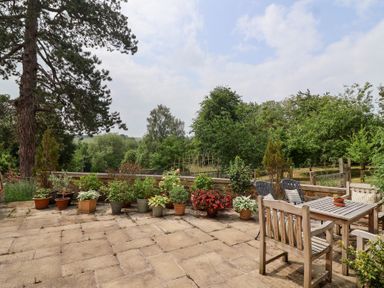 A garden with potted plants and patio furniture at Magdalen Cottage in Hook Norton