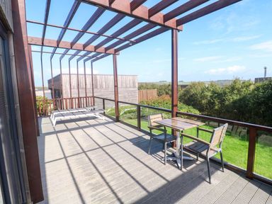 An outdoor area with a table and chairs under a pergola at Lodge 83, Gwel an Mor in Portreath