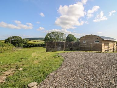An outdoor area with a wooden building and grassy landscape at Owl's Hollow in Chapel Lawn near Clun