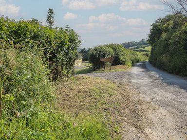 A gravel road bordered by hedges and a sign at Owl's Hollow Chapel Lawn near Clun