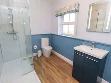 A bathroom with a shower, toilet, sink, and window at Linn Cottage in Hexham