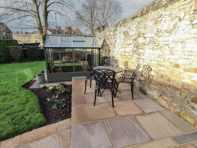 A garden with a greenhouse and seating area at Linn Cottage in Hexham