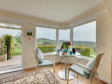 A conservatory with a table and chairs overlooking the garden at The Granary in Alnwick