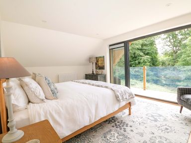 A bedroom with a bed and window overlooking a garden at Lakeside Lodge Witherenden Hill near Burwash