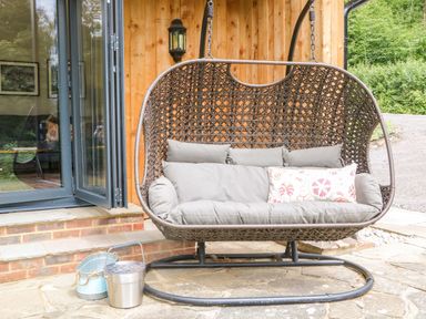 A hanging chair with cushions by a wooden wall at Lakeside Lodge in Witherenden Hill near Burwash
