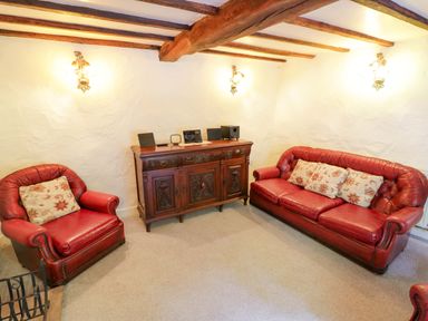 A living room with red furniture and a wooden cabinet at Fern Cottage
