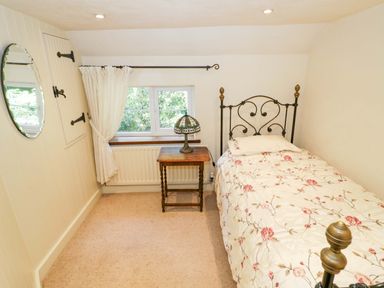 A bedroom with a bed, table, lamp, window and mirror at Fern Cottage