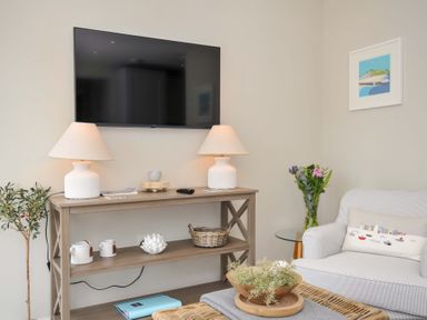 A living room with a television and lamps on a shelf at Evelyn in Looe
