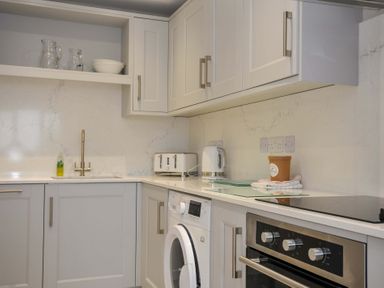 A kitchen with cabinets, sink, kettle, and washing machine at Evelyn in Looe