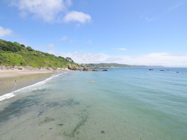 A beach with people swimming and boats in the ocean at Evelyn in Looe