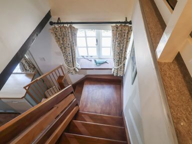 A staircase leading to a window with curtains at Buttercup in Blakeney, Norfolk
