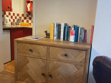 A bookcase with books and a kettle in a living room at The Bittern in Blakeney, Norfolk