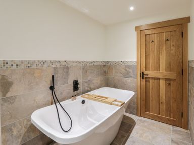 A bathroom with a bathtub and wooden door at The Barn at Sunny Barn in Brecon