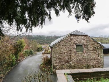 A stone building with a road and trees at The Barn at Sunny Barn in Brecon