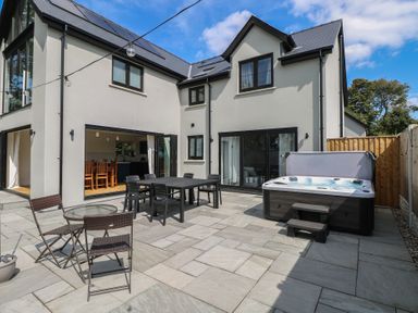 An outdoor patio with a dining set and hot tub at Ty Landsker in Houghton near Neyland