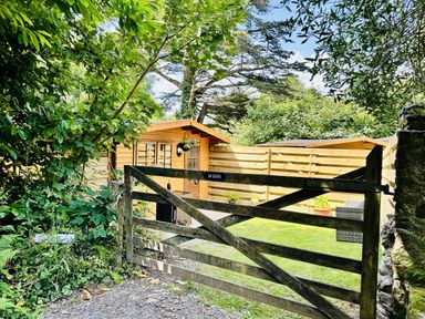 A wooden cabin behind a gate in an outdoor area at Harvey's Lodge, Lowertown, Helston