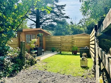 A garden with a wooden cabin and potted plants at Harvey's Lodge in Lowertown, Helston