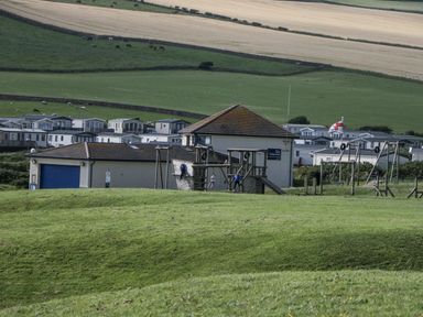 A playground structure with a building and caravans at Puffin St Bees