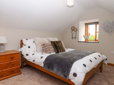 A bedroom with a bed, nightstand and window at Church Barn Sutcombe near Bradworthy