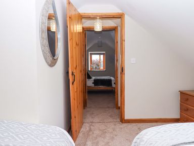 A door leading to a bedroom with a bed and window at Church Barn in Sutcombe near Bradworthy
