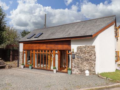 An exterior view of a building with large windows and stone wall at Church Barn Sutcombe near Bradworthy