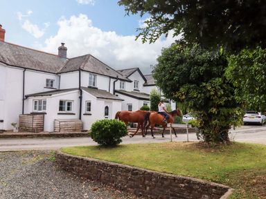 Two horses with riders and a house in the background at Church Barn Sutcombe near Bradworthy