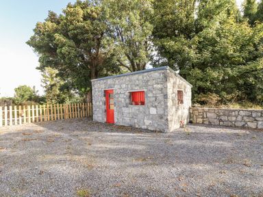 A stone building with a red door and window in an outdoor area at Kate's Cottage
