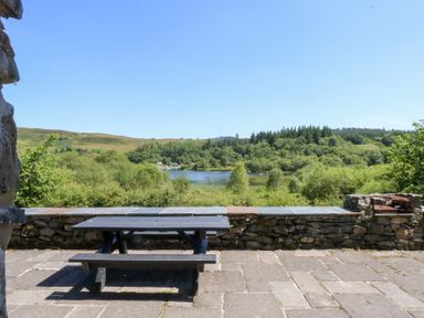 A table with benches overlooking a lake and trees at Ty Newydd