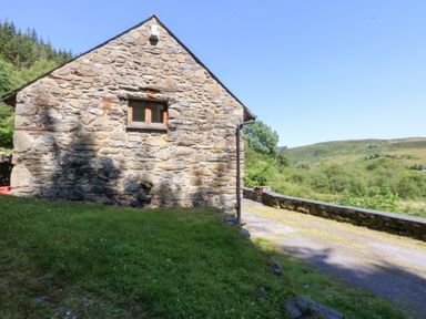 A stone building with a window and a road next to hills at Ty Newydd