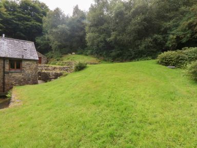 A stone building with a slate roof next to grass and trees at Ty Newydd in Llanrhychwyn near Llanrwst