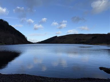 A lake surrounded by hills and trees at Ty Newydd in Llanrhychwyn near Llanrwst