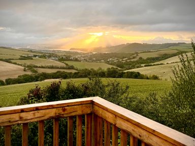 A sunset over hills and fields from a wooden balcony at Lowena Lodge Whitsand Bay Holiday Park near Millbrook